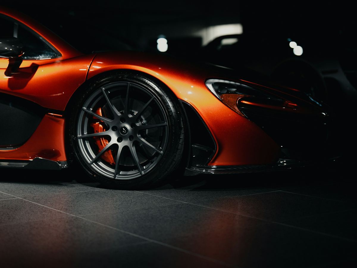 Supercar orange en studio, jante et ligne avant soulignées par la lumière sur fond noir